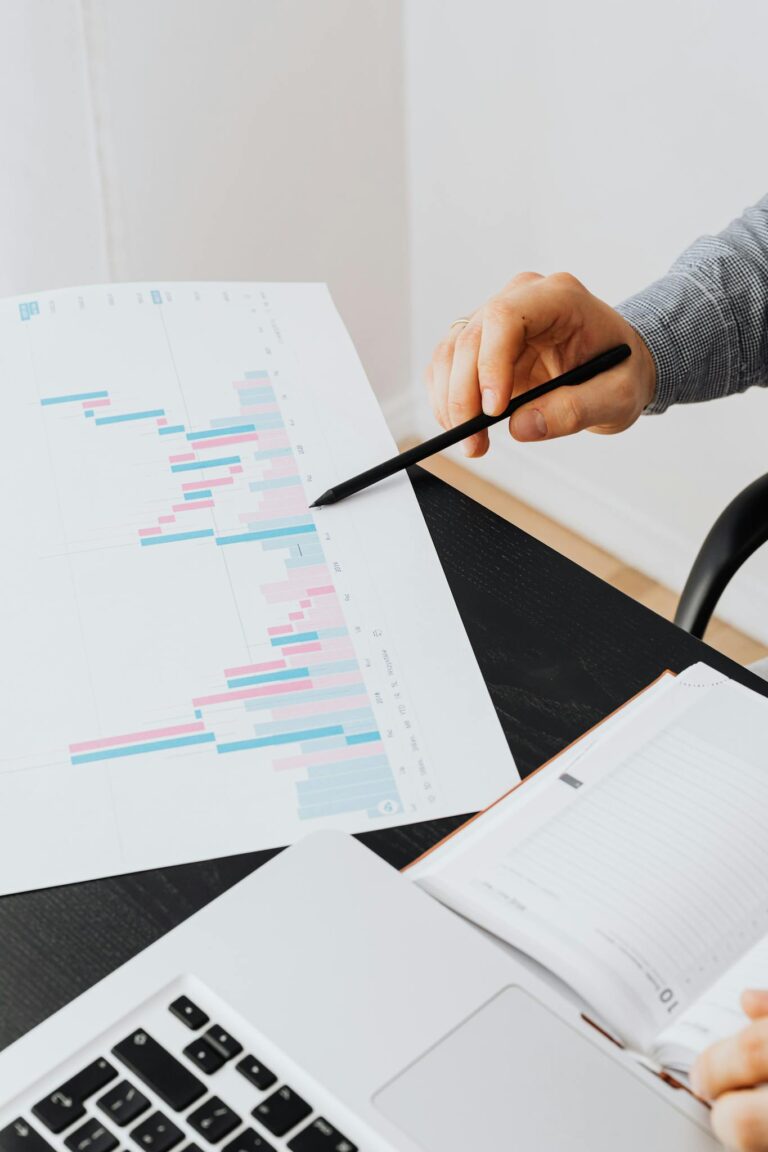 A professional analyzing data charts on paper with a laptop in an office setting.